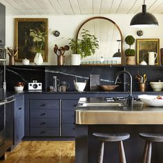 a kitchen with black cabinets and wooden flooring is pictured in this image, there are three stools at the counter