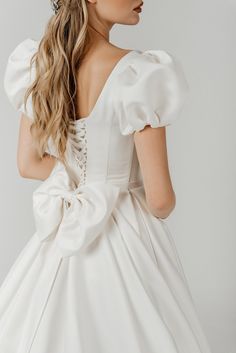 a woman wearing a white dress with a large bow in her hair, looking off to the side