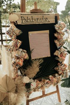 an easel decorated with pictures and feathers for a wedding ceremony at palabundia