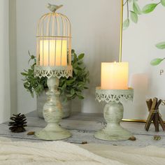 two candles sitting on top of a table next to a birdcage