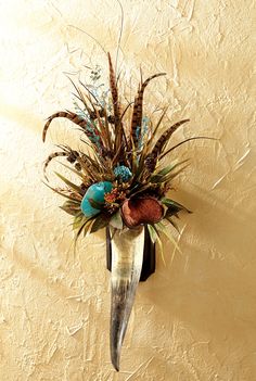 a wall mounted vase with feathers and flowers on it's side against a beige wall