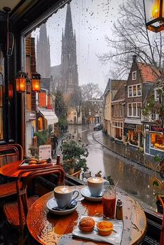 two cups of coffee sit on an outdoor table in front of a window overlooking a street