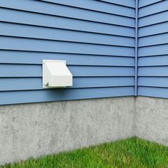 a wall mounted mailbox on the side of a blue and gray house with grass in front