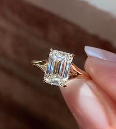 a close up of a person's hand holding a ring with an emerald stone