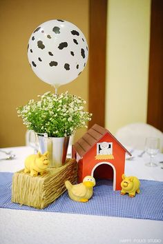 a table topped with a vase filled with flowers next to a small house and rubber ducks