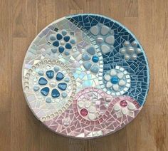 a blue and pink mosaic plate sitting on top of a wooden floor next to a wall