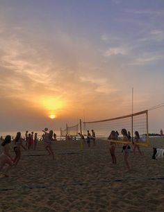 many people are playing volleyball on the beach as the sun is setting in the background