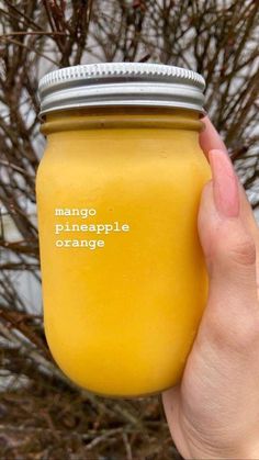 a person holding up a yellow mason jar with the words mango pineapple orange on it