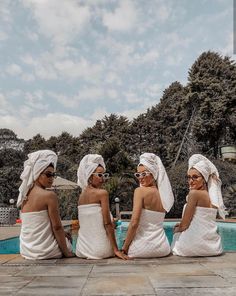 three women sitting next to each other near a swimming pool wearing towels on their heads