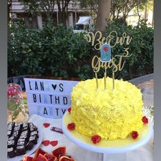 a yellow birthday cake sitting on top of a table next to other cakes and desserts