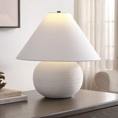 a white lamp sitting on top of a wooden table next to a book and vase