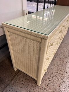 a white wicker chest with glass top sitting on the floor next to a window