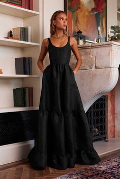 a woman standing in front of a fireplace wearing a black dress with tiered ruffles