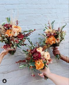 three hands holding flowers against a brick wall