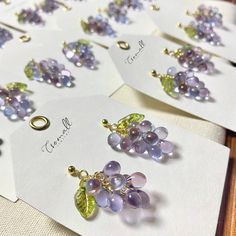 several earrings are displayed on white cards with green and purple leaves attached to them, sitting on a table