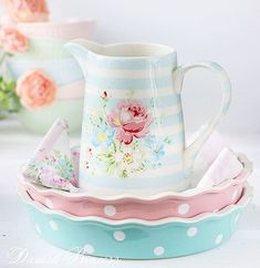 a pitcher sitting on top of a blue and white bowl next to other bowls filled with flowers