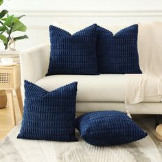 two blue pillows sitting on top of a white couch in front of a potted plant