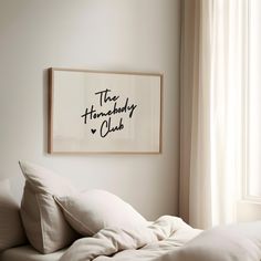 a bed with white sheets and pillows in front of a framed poster on the wall