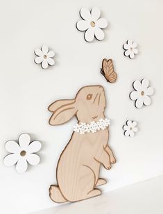 a wooden cutout of a rabbit with flowers and butterflies in the background on a white wall