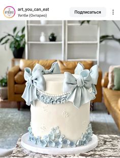 a white cake with blue flowers and bows on the top is sitting on a table in front of a couch