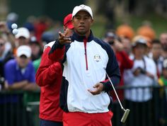 tiger woods waves to the crowd while holding his golf club