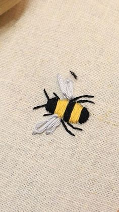 a yellow and black bee embroidered onto a piece of linen with some thread on it