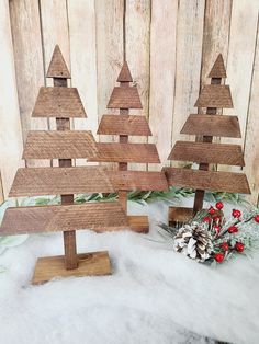 three wooden christmas trees sitting on top of snow covered ground next to a pine cone