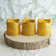 three gold glitter candles sitting on top of a wooden slice