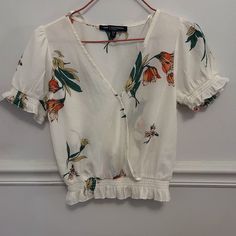 White Blouse This Short Sleeve White Blouse Has Flowers In Yellow And Orange With Green Leaves. It Is In A V-Neck Style And Has A Small Snap For Closure. It Also Has Puff Sleeves And An Elastic Ruffle At The Hem. 97% Polyester, 3% Spandex Size Xs Length Measures At 18 Inches Shoulder Width Measures At 12.5 Inches Chest Width Measures At 14.5 Inches Inches Measurements Are Approximate. Nwot (New Without Tags) Smoke Free And Pet Free Home! Cheap Summer Button-up Blouse, Short Sleeve White Blouse, Pink Chiffon Blouse, Light Green Blouse, White Short Sleeve Blouse, Black Shirts Women, One Clothing, Beautiful Blouses, Green Blouse