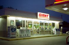 an old fashioned gas station at night with the lights on and ice machines in front