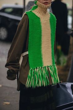 a woman wearing a green and white sweater with fringes on her shoulders is walking down the street