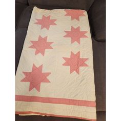 a pink and white quilt with red stars on the bottom is sitting on a couch