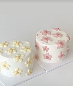 two white cakes with pink and yellow flowers on them are sitting on a counter top