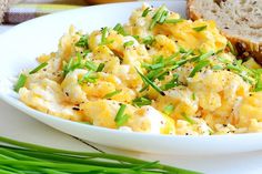 an egg salad on a white plate with bread and green onions next to it, ready to be eaten