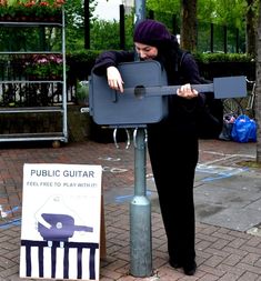 a woman standing next to a street sign with a guitar strapped to it's back