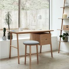 a desk and chair in front of a window with potted plants on the windowsill