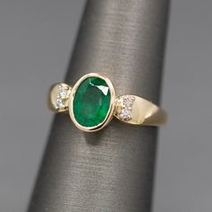 This richly hued ring is just the natural emerald you've been looking for. Sitting low on the finger and well protected by the bezel setting, this emerald glows green. The stone measures 8mm x 6mm, weighing 1.02ct. It is flanked by two round prong set diamonds on the shoulders, just enough sparkle to flash! The diamonds are F/G color and VS clarity, totaling 0.08ctw. The ring is crafted in solid 14k yellow gold and weighs 3.78g. It is currently a size 5.5 and can be resized before shipment for a Bezel Set Diamond, Natural Emerald, Emerald Ring, Bezel Setting, Prong Setting, Statement Rings, Emerald, Flash, Diamonds