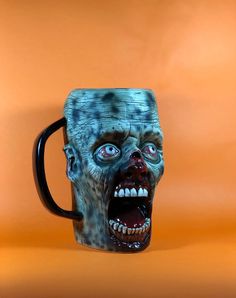 a ceramic mug with an evil face on the front and sides, sitting in front of an orange background