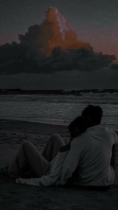 two people are sitting on the beach watching the sun go down and clouds in the sky