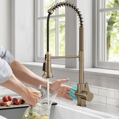 a woman washing her hands under a kitchen faucet next to a sink filled with fruit