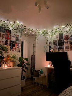 a bedroom decorated with plants and pictures on the wall, lights strung from the ceiling