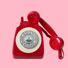 an old red telephone on a pink background