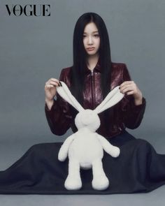 a woman sitting on the ground with a stuffed rabbit in front of her, wearing a leather jacket