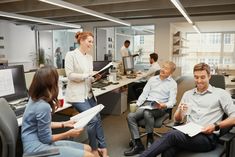 people in an office having a discussion with each other and one man is holding papers