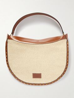 Isabel Marant sizes up its signature 'Oskan' bag to unexpected proportions. Made from raffia, it has a slouchy, curved shape outlined with gold-tone studs and camel leather to match the logo stamp. The wide strap fits comfortably over your shoulder, and the canvas-lined interior has enough space for your tablet, water bottle and hardcover book. Designer Top Handle Straw Bag For Errands, Luxury Top Handle Straw Bag For Errands, Designer Bags With Leather Handles In Natural Color, Designer Leather Straw Bag, Luxury Woven Bags For Errands, Luxury Woven Bag For Errands, Designer Woven Bags In Natural Color, Luxury Leather Woven Shoulder Bag, Designer Natural Leather Shoulder Bag