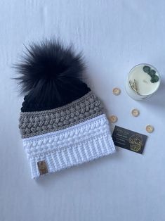 a knitted hat with a black pom - pom sits next to some buttons