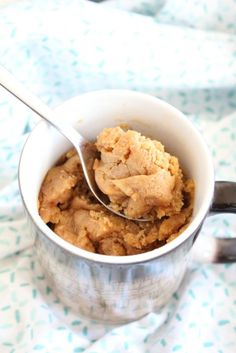 a spoon in a cup filled with food on top of a cloth covered tablecloth