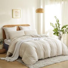 a bed with white comforter and pillows in a room next to a potted plant