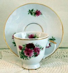 a tea cup and saucer with pink flowers on it sitting on a doily