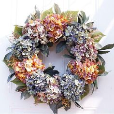 a wreath with purple and orange flowers hanging on a white door frame in the sun